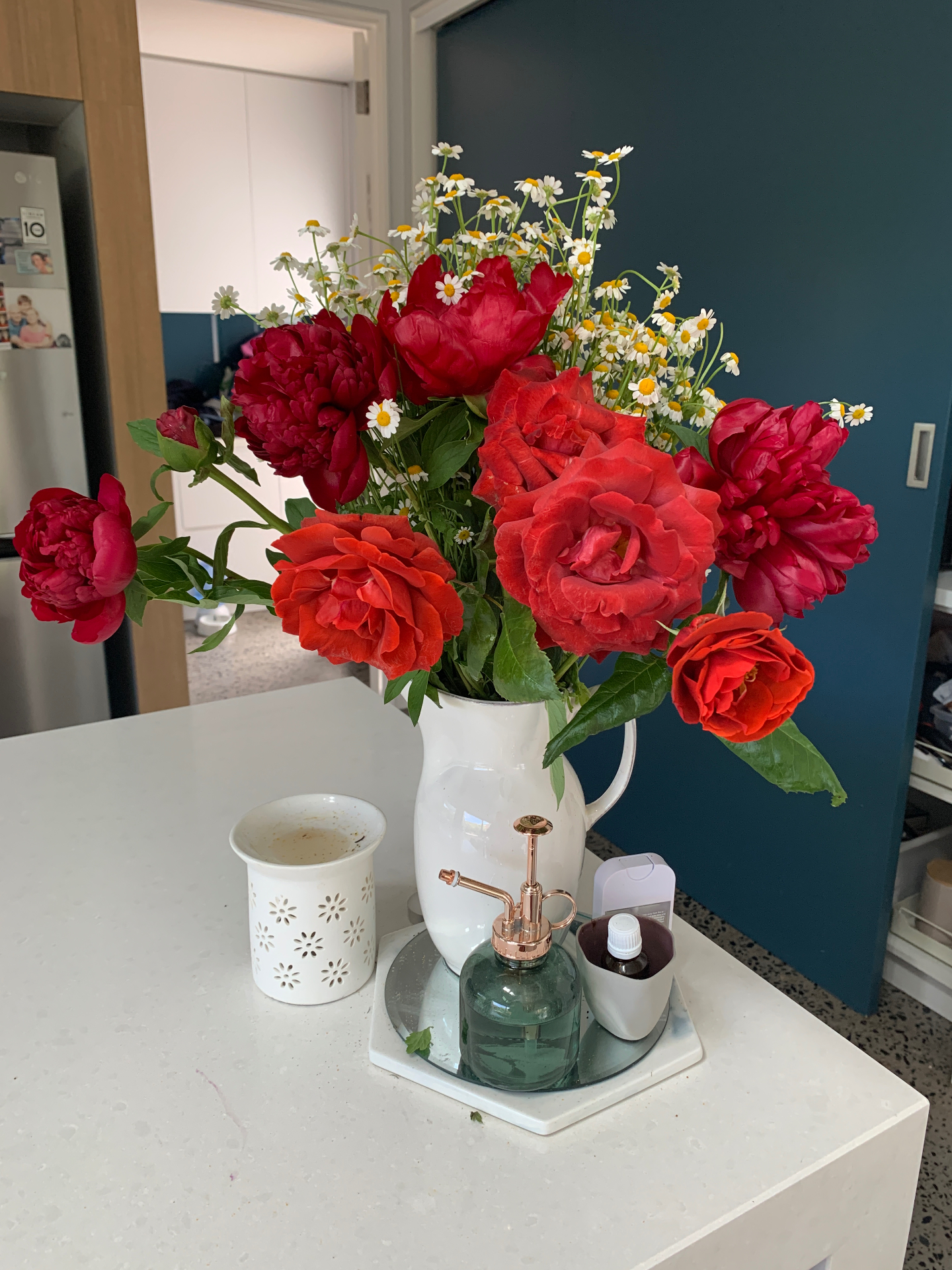 Deep red roses with chamomile daisies in a white pitcher